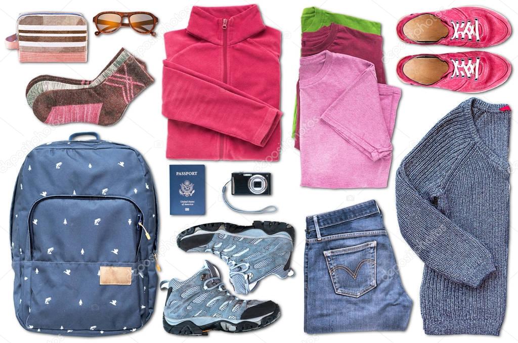 View from above of unisex travel essentials such as a backpack, shoes, clothes, a digital camera, sunglasses, a cosmetic bag, a passport (USA), organized to fill the space on the white background