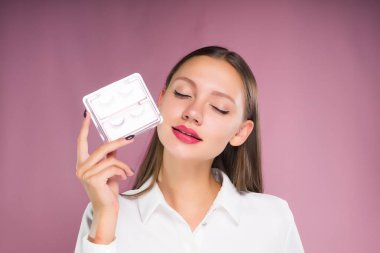 Gözleri kapalı güzel bir kızla bir kutu sahte kirpik ile onun elinde tutar.