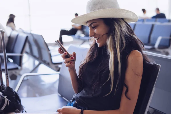 Jovem de chapéu senta-se com um telefone no aeroporto — Fotografia de Stock