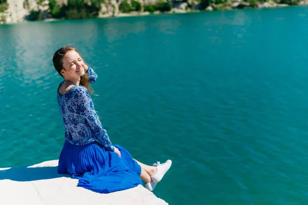 Красива дівчина в блакитній сукні посміхається на березі озера — стокове фото