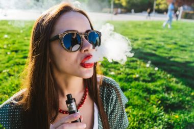 Mutlu moda gülümseyen kadın güneş gözlüğü vape Street, duman Sigara