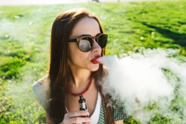 Mutlu moda gülümseyen kadın güneş gözlüğü vape Street, duman Sigara