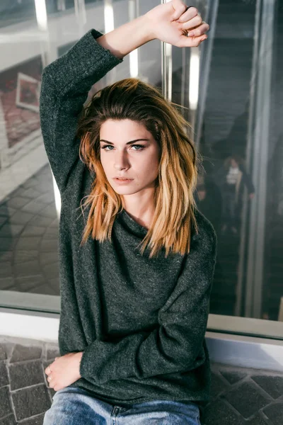 Genç sarışın bir kadın bir cam kapı oturur