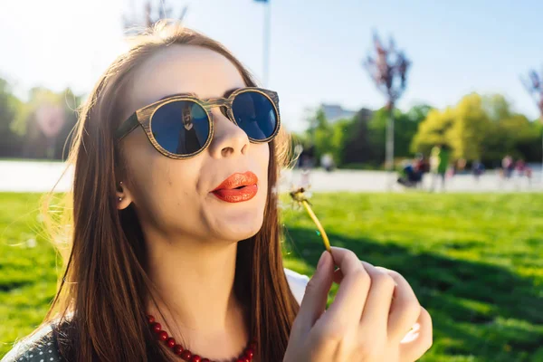 Srandovní usměvavý šťastná žena v sluneční brýle foukání Pampeliška — Stock fotografie