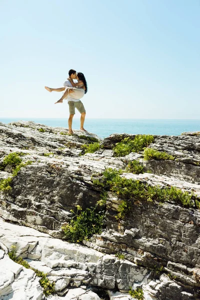 Un uomo tiene una ragazza tra le braccia in lontananza sullo sfondo dell'oceano — Foto Stock