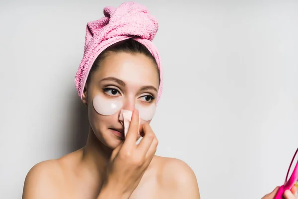 Jovem mulher bonita com uma máscara sob os olhos olha para si mesma no espelho, limpa a pele — Fotografia de Stock