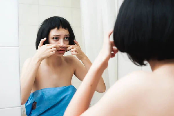 Дівчинка-підліток дивиться на своє обличчя у дзеркало у ванній кімнаті і стискає прищики — стокове фото