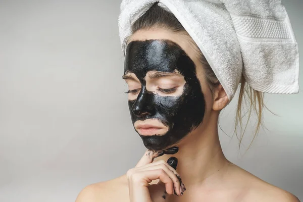 女人的皮肤护理，化妆品黑面具的脸上。在头上的毛巾 — 图库照片