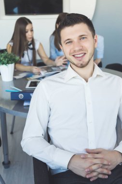 Ofiste oturan ve kameraya, işçiler arka plan üzerinde seyir rahat emin iş adamı. Öğrencilerin çalışma