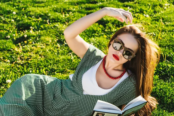 Okuma kadınla çimenlerin üzerinde. Öğrenci park, güneş gözlüğü hazırlanıyor