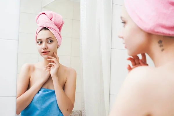 Молода красива жінка дивиться і торкається її обличчя у дзеркалі у ванній — стокове фото