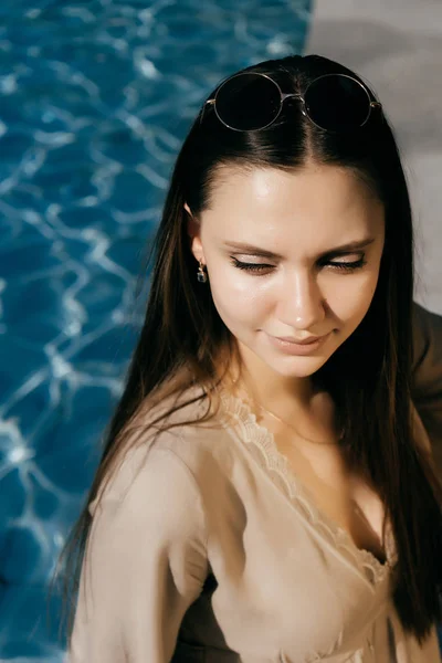 Joven mujer de moda sentada cerca de la piscina, sonriendo — Foto de Stock