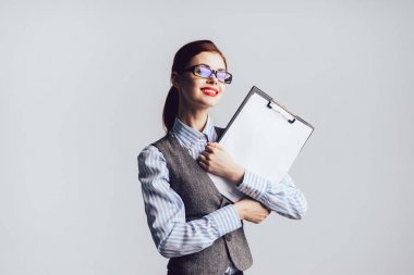 Güvenle gülümseyen elinde, gözlük ve kağıt ile bir takım elbise giyen bir temiz güzel genç iş kadını