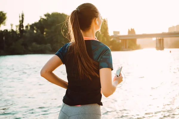 Sports woman runner runs, view from behind, holds smartphone