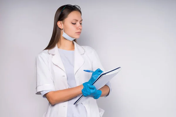 En kvinnlig läkare skriver något i en anteckningsbok, är klädd i morgonrock, en läkare — Stockfoto