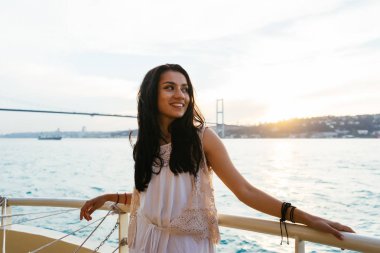 Genç kız gezgin bir yatta seyir ederken rahatlatır, gün batımı ve okyanus bakarak, arka plan üzerinde köprü. İstanbul 'un boğaz köprü
