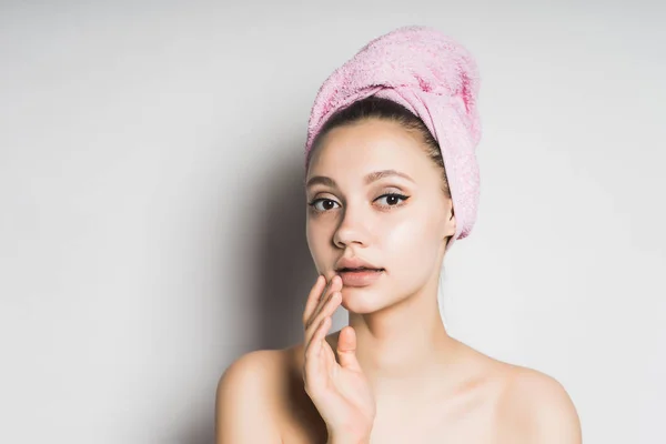 Загадочная девушка с розовым полотенцем на голове на белом фоне на спа-процедуры — стоковое фото