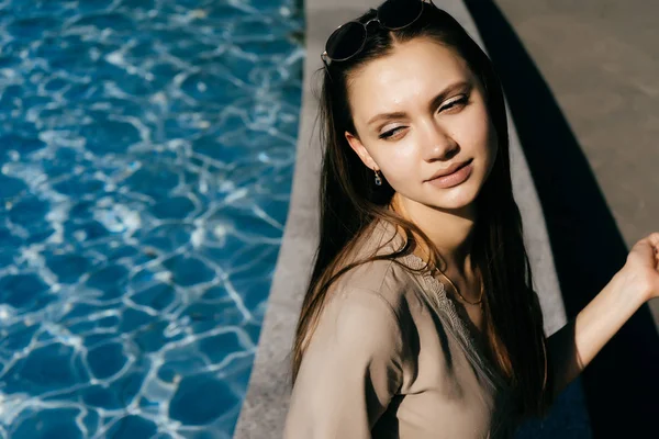 Ragazza con i capelli lunghi seduta a bordo piscina e guardando altrove — Foto Stock