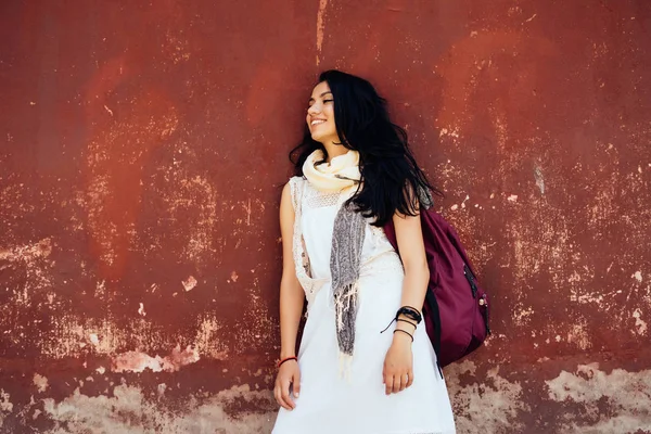 Kız öğrenci bir sırt çantası ile eski duvarın, üniversite öğrencisi tatil yanında ayakta rahatlatır