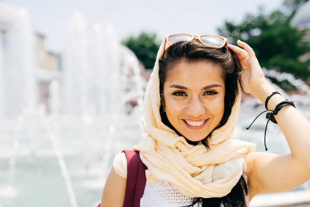 Close-up portrait of a happy young Muslim woman in a scarf and glasses. Summer travel, exchange student