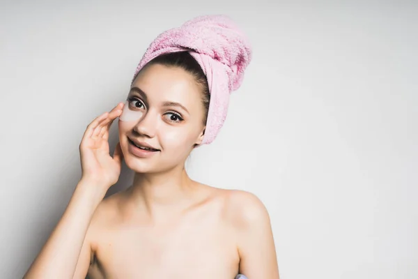 Schönes Mädchen mit sauberer Haut und einem Handtuch auf dem Kopf und einer Maske unter den Augen — Stockfoto