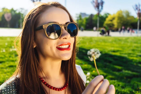Смешная улыбающаяся счастливая женщина в солнечных очках, дующая в одуванчик — стоковое фото