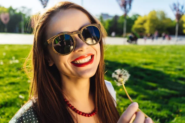 Funny smiling happy woman in sunglasses blowing dandelion — Stock Photo, Image