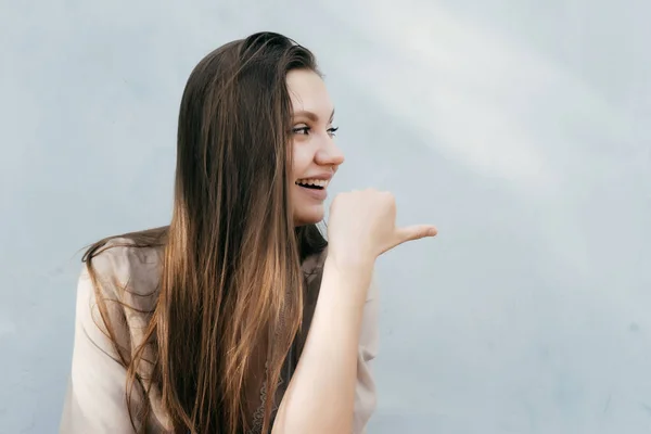 Chica con el pelo largo sonríe y señala su dedo hacia un lado — Foto de Stock