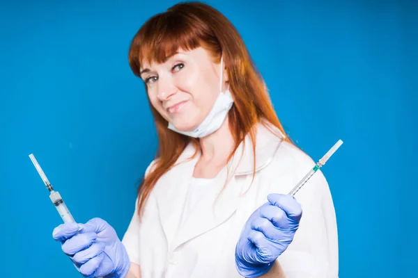 Enfermera roja sosteniendo dos inyecciones en las manos, aislada sobre fondo azul — Foto de Stock
