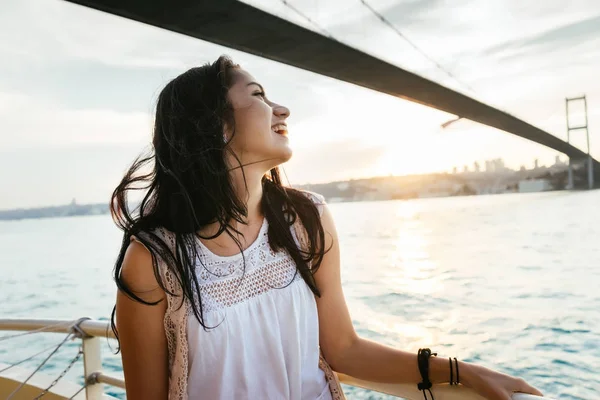 Ritratto di una bella ragazza latina su uno yacht al tramonto nuota sotto un ponte moderno e ride, un viaggio in traghetto — Foto Stock