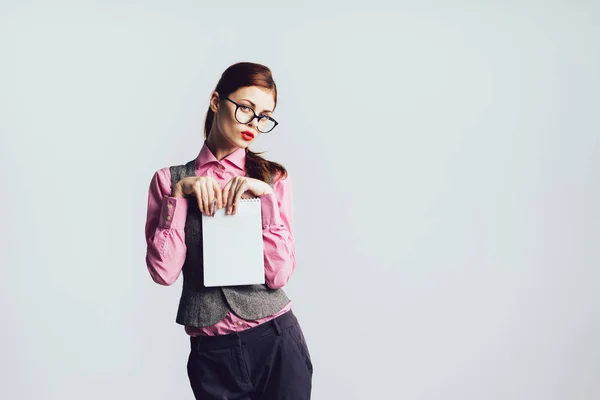 Ein junges Sekretärmädchen mit Brille und rosa Hemd hält eine Akte auf grauem Hintergrund — Stockfoto