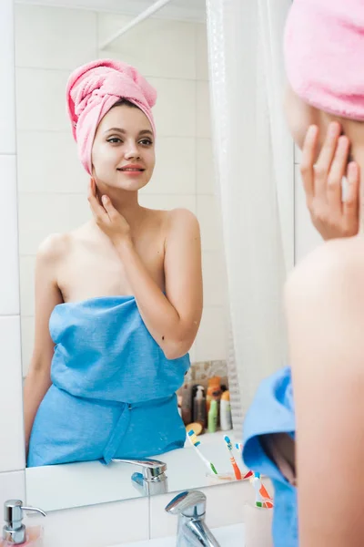 Fille souriante avec une serviette sur la tête dans un peignoir se regarde dans le miroir — Photo