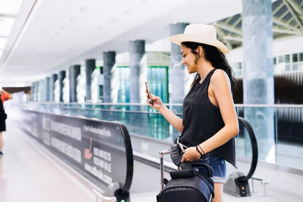 Travel woman using smartphone at airport. Young eastern traveler checking boarding time with mobile phone app in terminal or train station. Tourist on vacation. — Stock Photo, Image