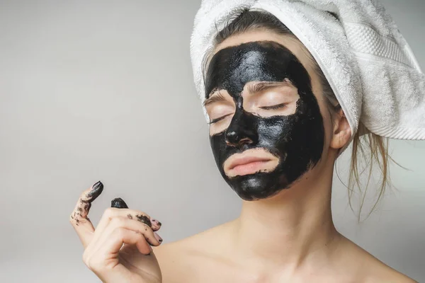 女人的皮肤护理，化妆品黑面具的脸上。在头上的毛巾 — 图库照片