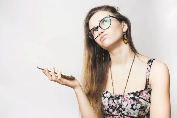 Pensando menina com óculos e um vestido bonito está segurando um telefone — Fotografia de Stock