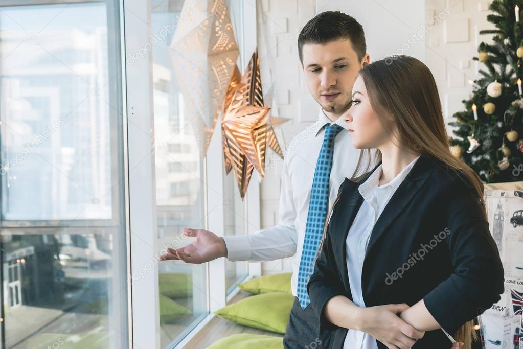 girl in suit looks out the window, man shows woman the view from the window, office