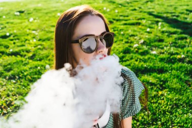 Mutlu moda gülümseyen kadın güneş gözlüğü vape Street, duman Sigara