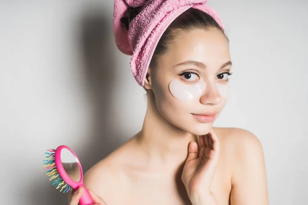 Jolie fille avec une serviette rose sur le gant tient un peigne multicolore sur un fond blanc — Photo