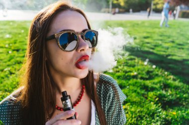 Mutlu moda gülümseyen kadın güneş gözlüğü vape Street, duman Sigara