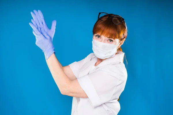 En kvinna i medicinska kläder bär en mask och handskar sträckte armarna upp, isolerade — Stockfoto