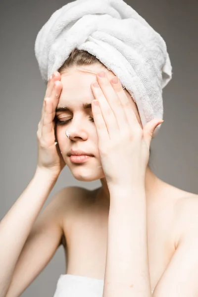 Милая девушка после душа с полотенцем на голове кладет крем на лицо — стоковое фото