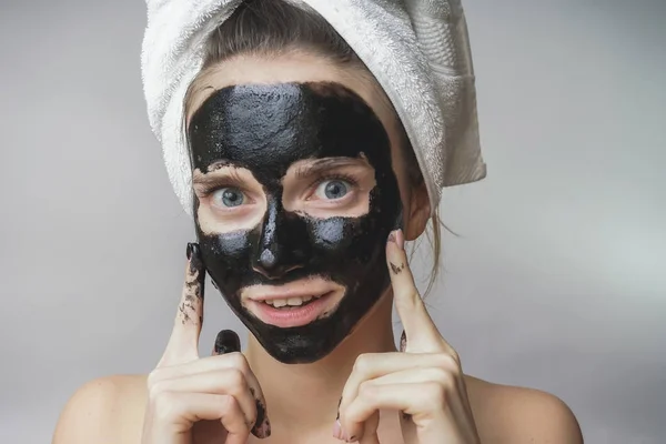 Lycklig glada kvinna applicera svart mask på ansiktet. Hud vård, ren porer, exfoliering — Stockfoto