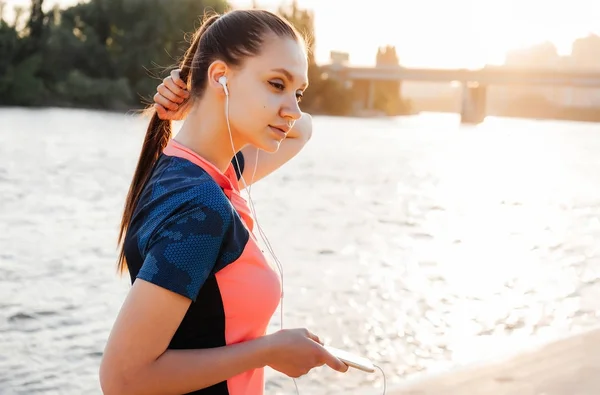 Flicka med en vacker lång svans lyssnar på musik efter jogging på Älvstranden — Stockfoto