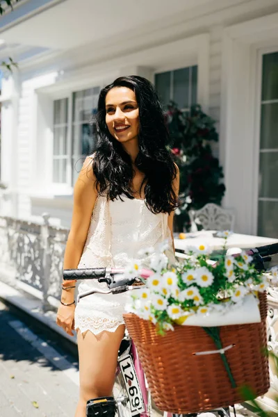Backet çiçek, eski evin arka plan ile bisiklet üzerinde oturan büyüleyici kadın