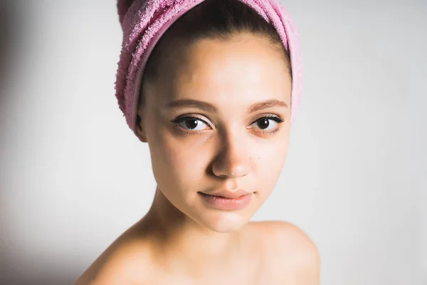 Όμορφο και χαριτωμένο κορίτσι με μια ροζ πετσέτα στο κεφάλι κοιτάζει την κάμερα, απομονωμένο — Φωτογραφία Αρχείου