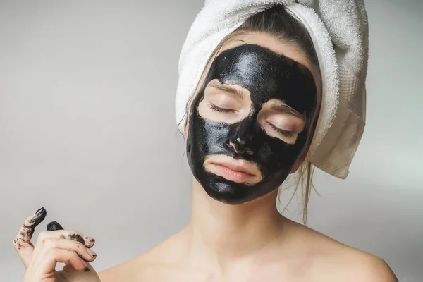 Γυναίκα φροντίδα του δέρματος, καλλυντικά μαύρη μάσκα στο πρόσωπο. Πετσέτα στο κεφάλι — Φωτογραφία Αρχείου