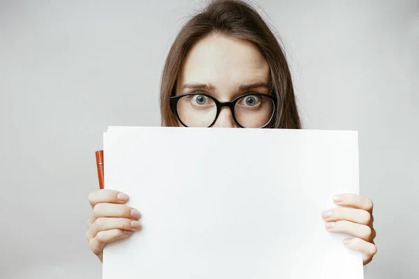 Verblüfftes Gesicht Frau versteckt sich hinter Papier, ein verängstigtes Mädchen lugt hinter einem Blatt a4 hervor — Stockfoto