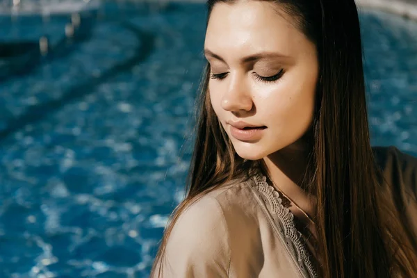Söt och vacker flicka sitter vid poolen och tittar bort — Stockfoto