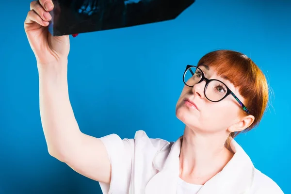 Rothaarige Krankenschwester untersucht vorsichtig ein Röntgenbild, isoliert auf blauem Hintergrund — Stockfoto