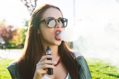 Mutlu moda gülümseyen kadın güneş gözlüğü vape Street, duman Sigara